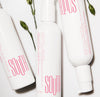 Three bottles of SOUTH intimate cleanser, unscented, shot from above with miniature roses