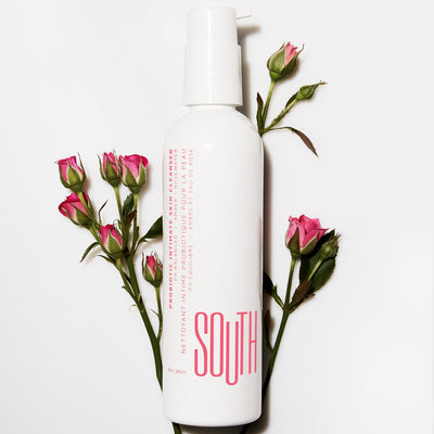 Bottle of SOUTH intimate cleanser shot from above, surrounded by miniature pink roses