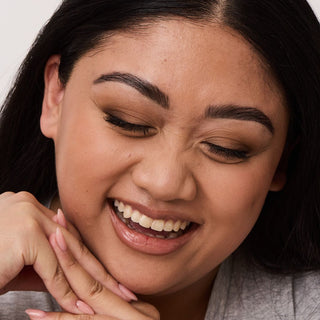 Close up portrait image of a woman laughing and looking down, her brows are newly shaped, tinted, and laminated from WAXON's Brow Boost Brow Service