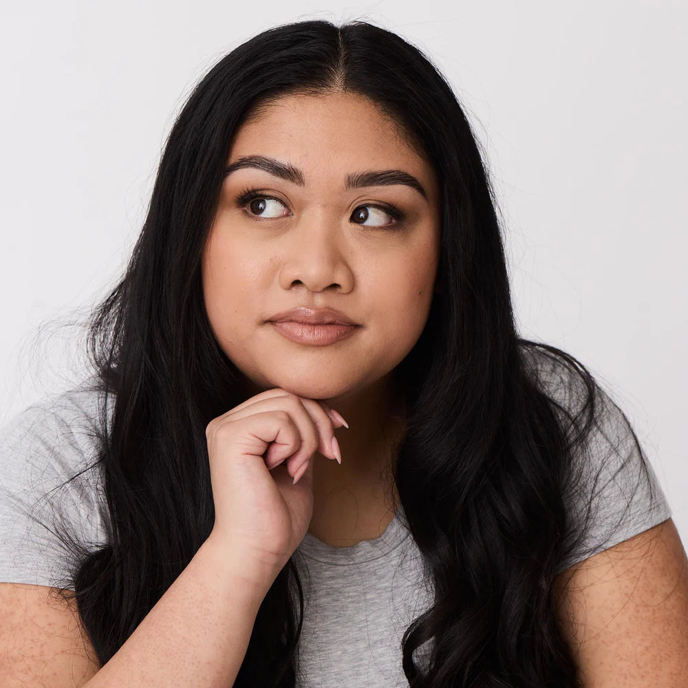 Portrait of a dark haired woman with freshly waxed, tinted, laminated, shaped brows. She is staring off to the side of the screen with one hand on her chin.