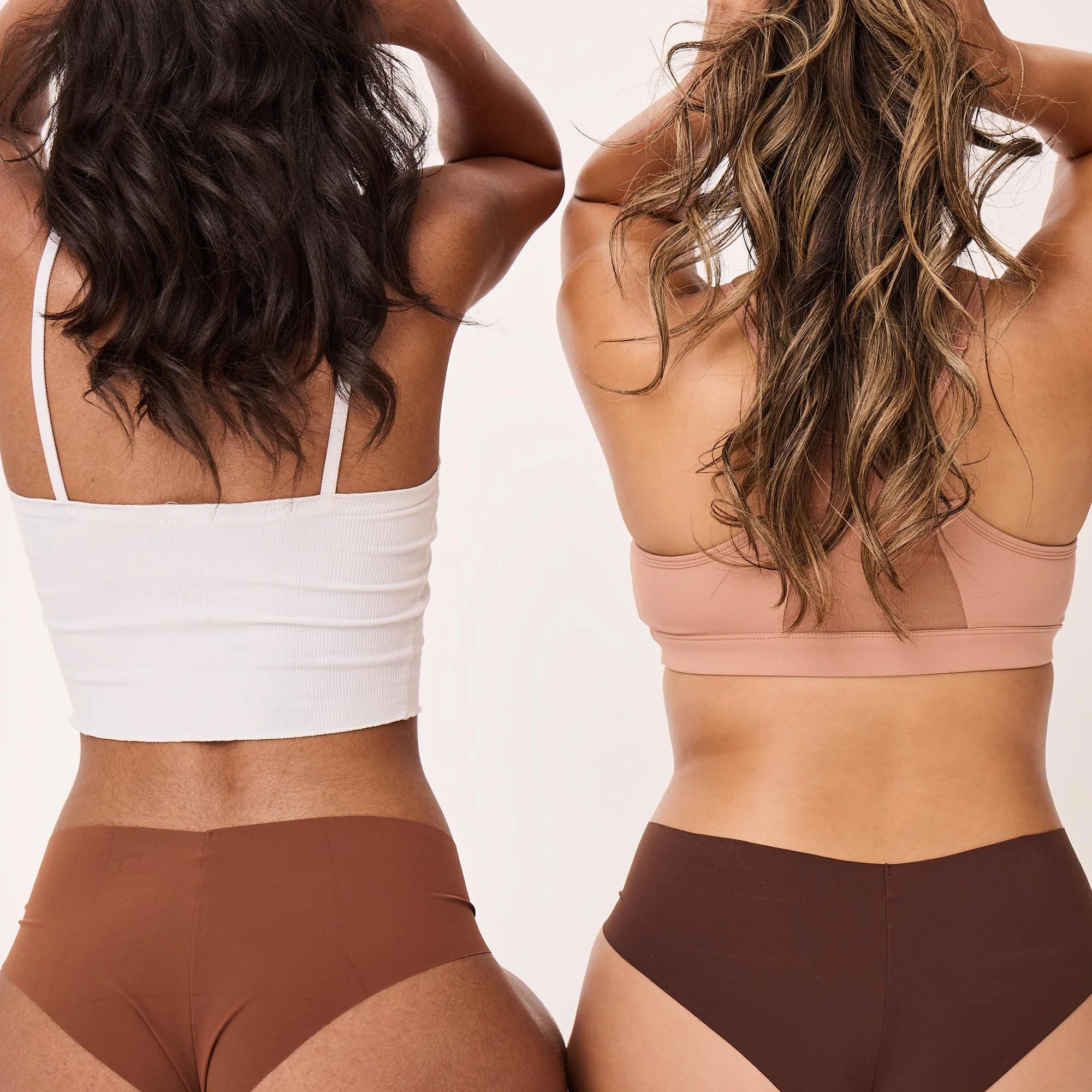 Two women wearing sports bras and high-waisted leggings against a plain background. Their skin is smooth and free of hair.