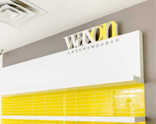 Interior image of a WAXON Laser + Waxbar, the scene shows the back wall being Guest Services with yellow tiles and the WAXON word mark logo.