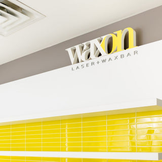 WAXON Laser + Waxbar interior wall behind guest services. The wall is tiled in WAXON yellow and grey brand colours.