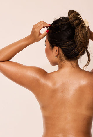 An image of a woman with her back to the camera, she has glowing skin from using BARE body oil from Body by WAXON.