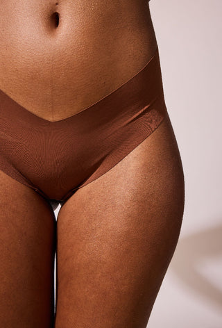 Close up shot of a woman's stomach and legs. The woman has smooth glowing skin and is wearing neutral coloured underwear.
