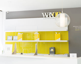 WAXON Laser + Waxbar Guest Services desk, behind is a yellow tiled wall with a grey accent wall.
